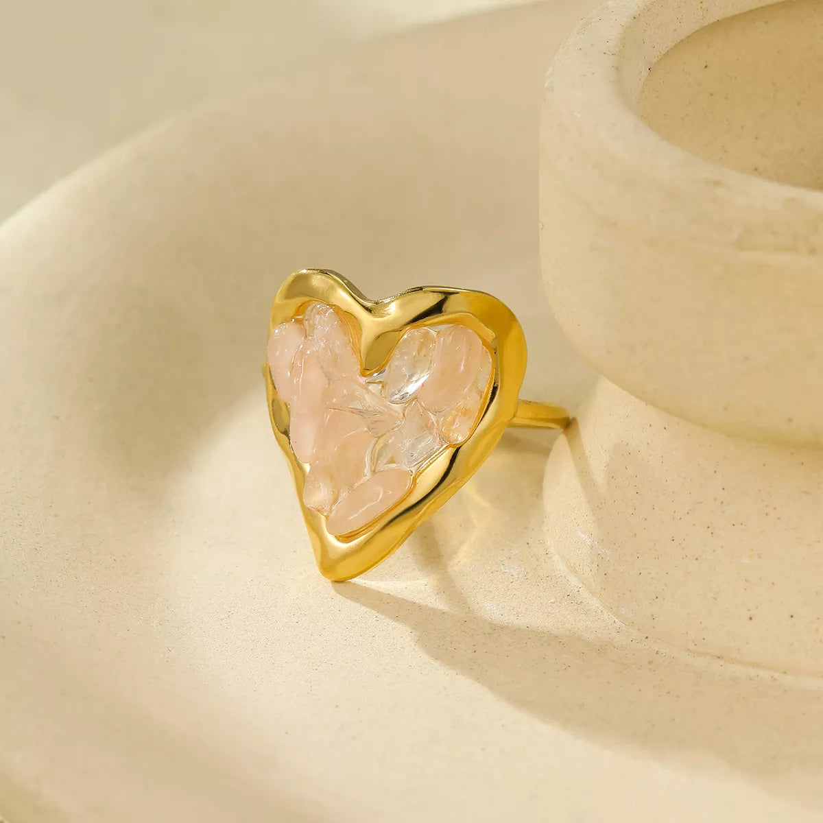 Gold heart ring featuring blush pink rose quartz crystals, resting in a cream dish.