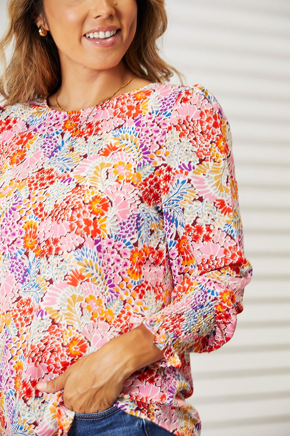 Woman wearing a vibrant long-sleeve floral print blouse with puff sleeves and smocked cuffs.