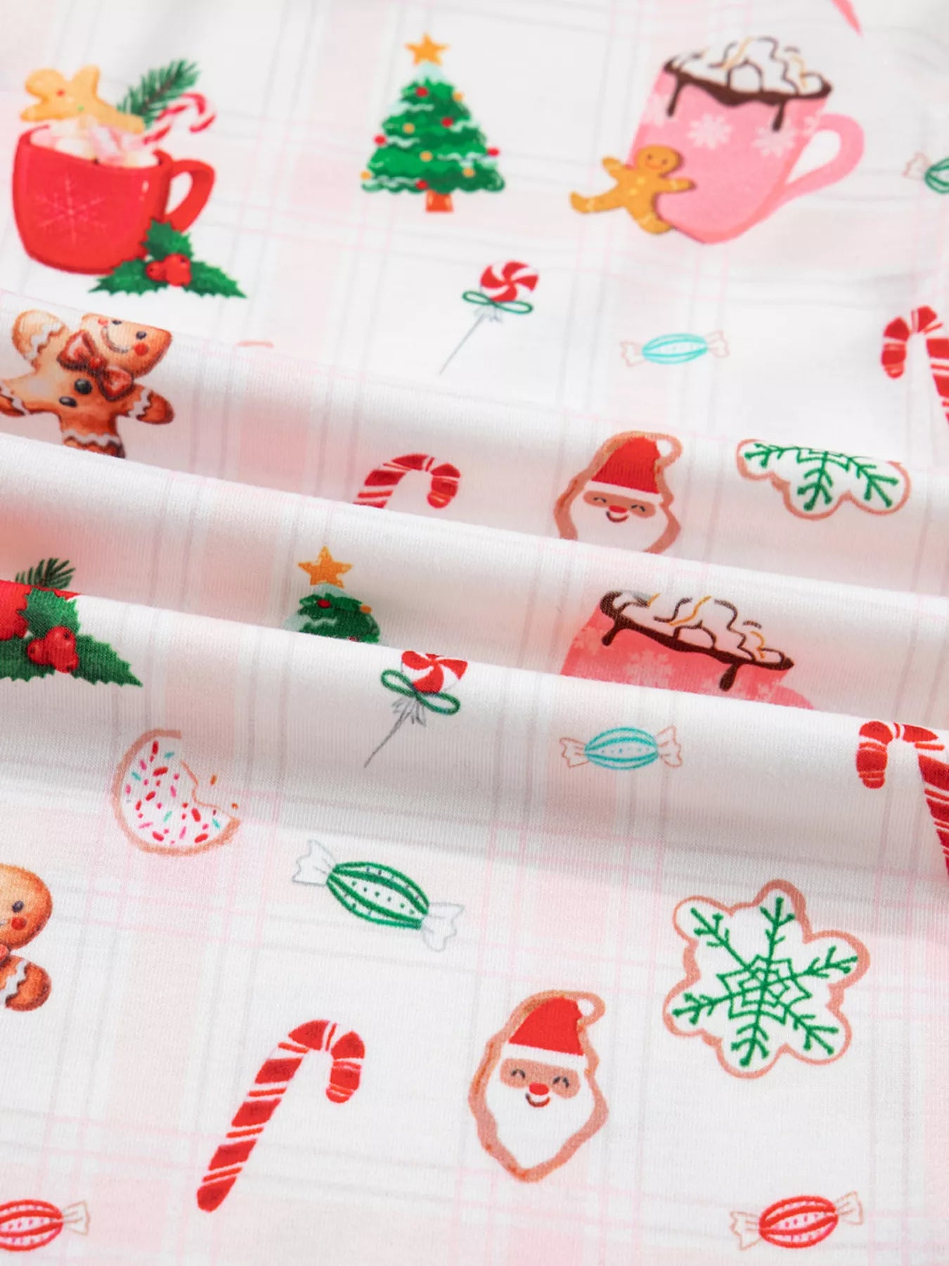 Close-up of holiday printed pajama pants featuring candy canes, cocoa mugs, gingerbread cookies, and Santa motifs.