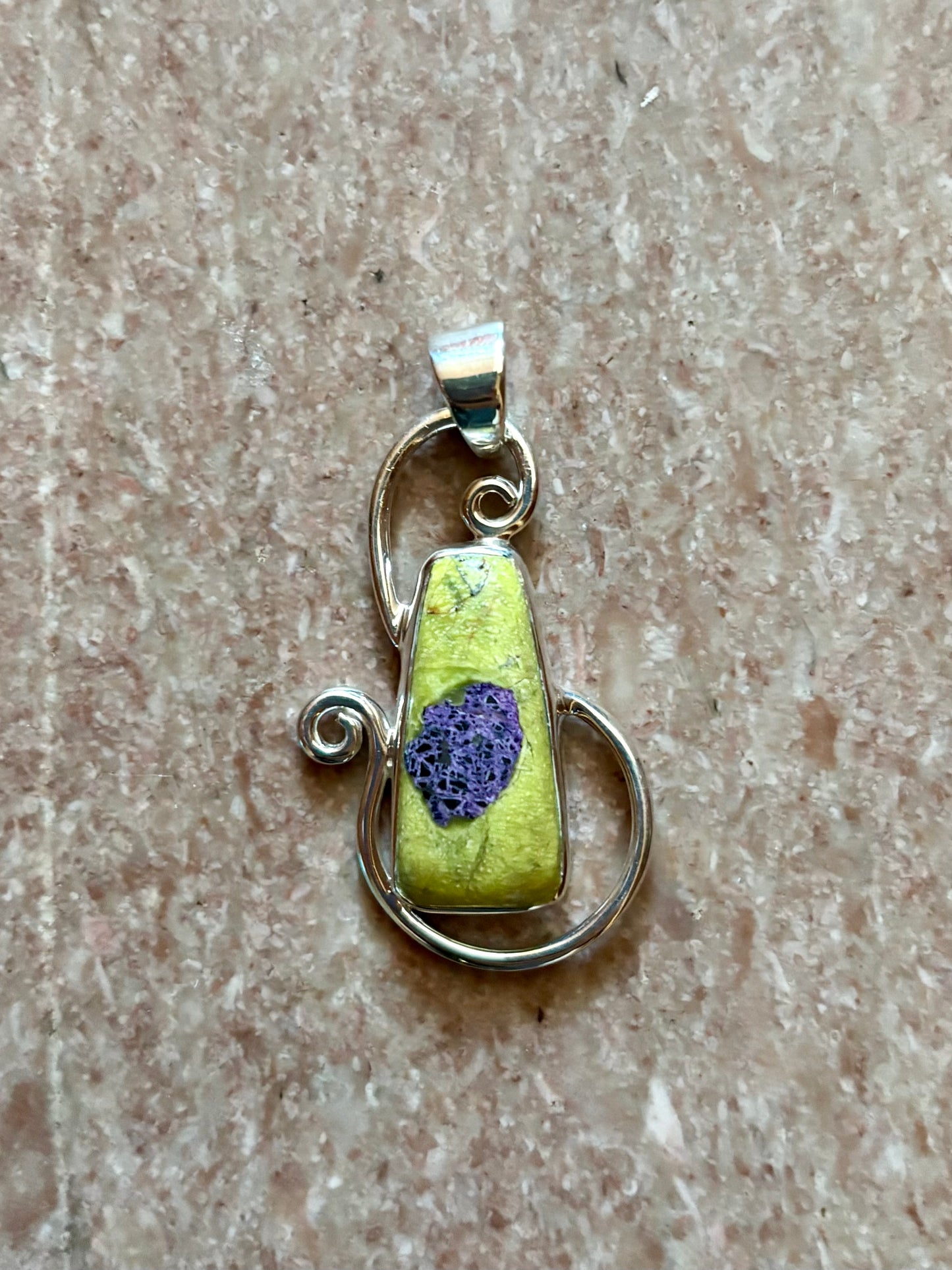 Green Alantiste crystal pendant with natural purple inclusion wrapped in silver wire on wooden surface