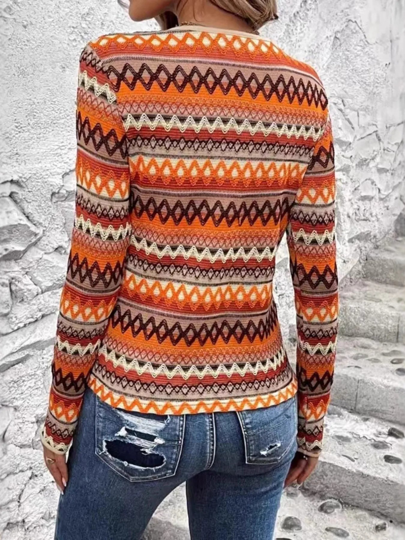 Model wearing Autumn Ember Knit Top with long sleeves and bold geometric knit-style pattern in warm autumn tones of orange, brown, and cream.