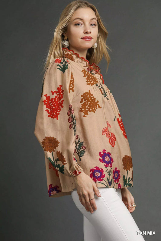 Model wearing a beige floral blouse with scalloped red-trim neckline and long puff sleeves, paired with white pants.