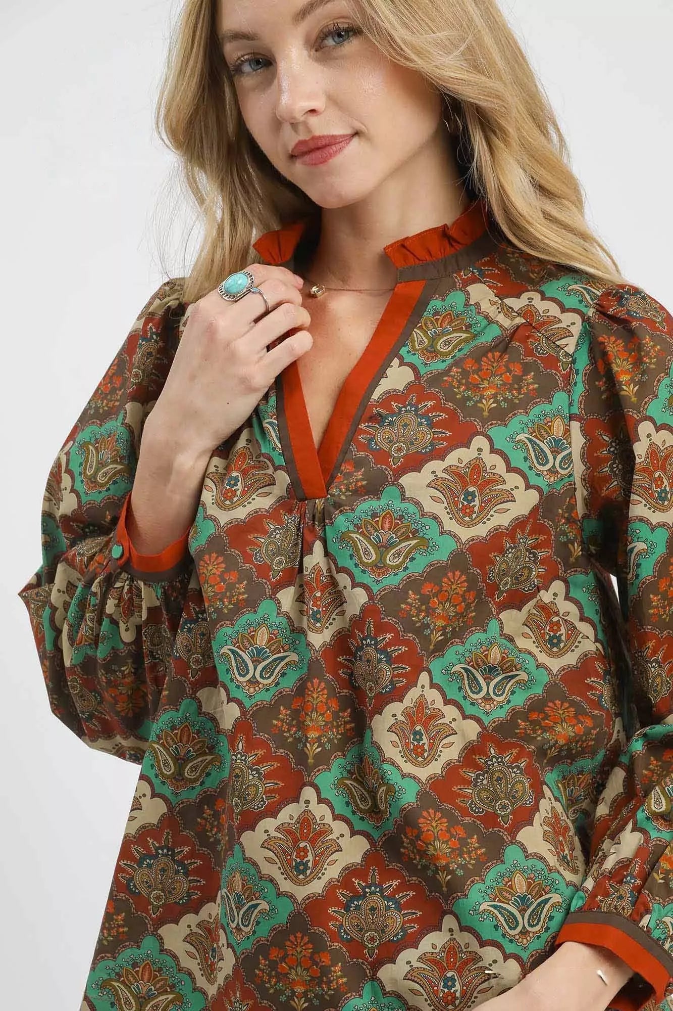 Woman wearing an abstract print ruffle neck top with earthy tones and long sleeves.