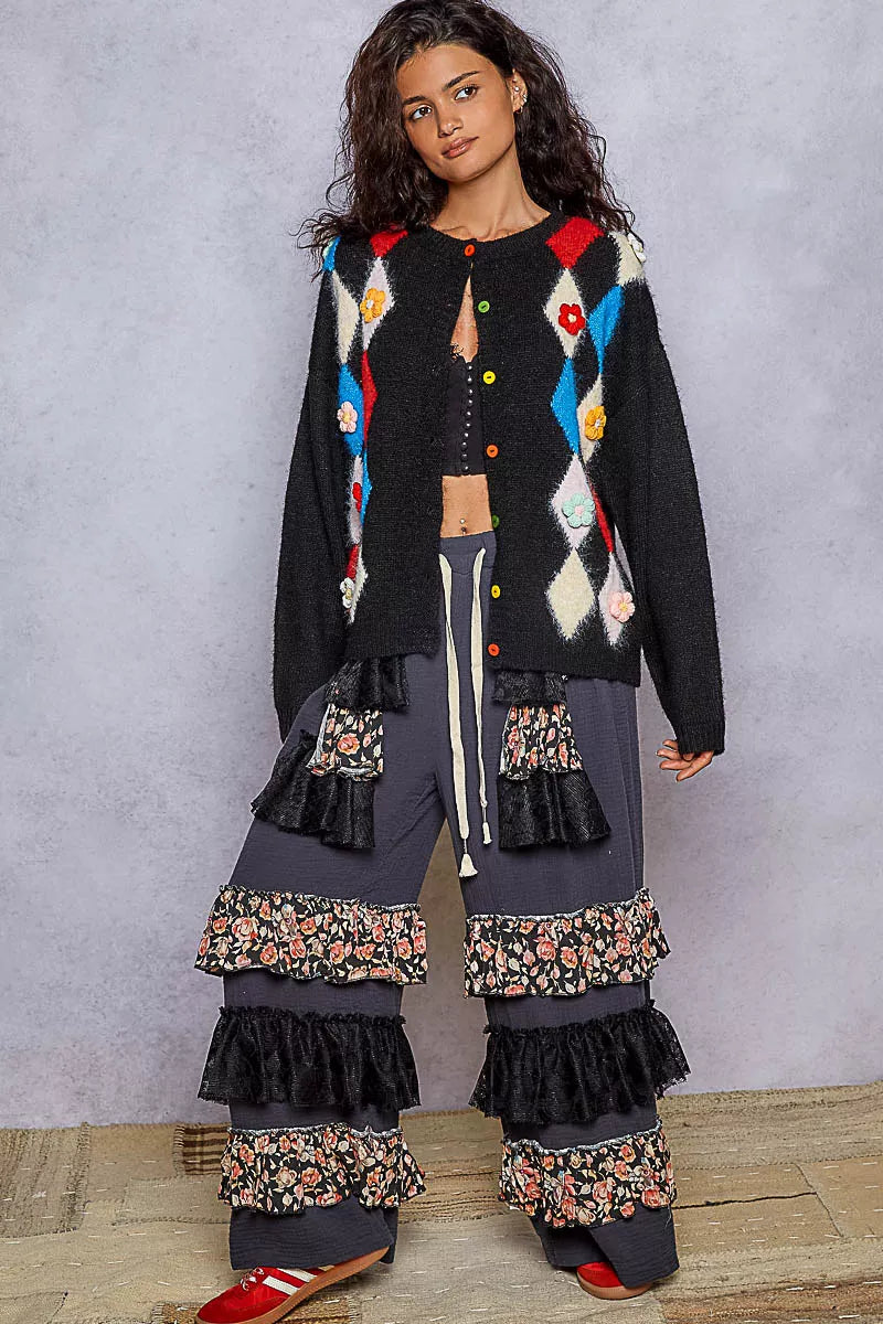 Front view of model wearing black cardigan with colorful argyle pattern and floral accents