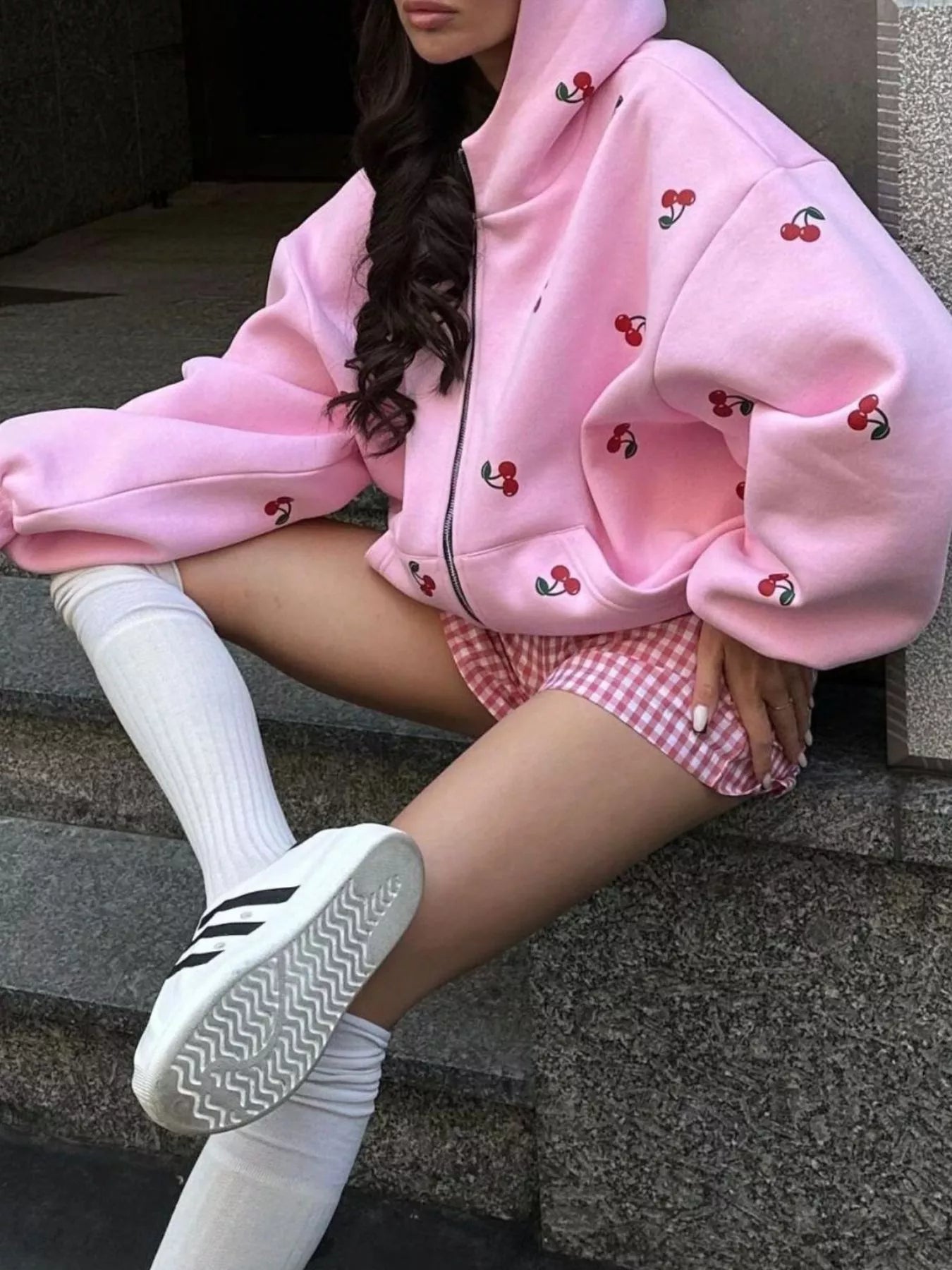 Model wearing a pink oversized zip hoodie with cherry embroidery, paired with gingham shorts for a playful casual outfit.