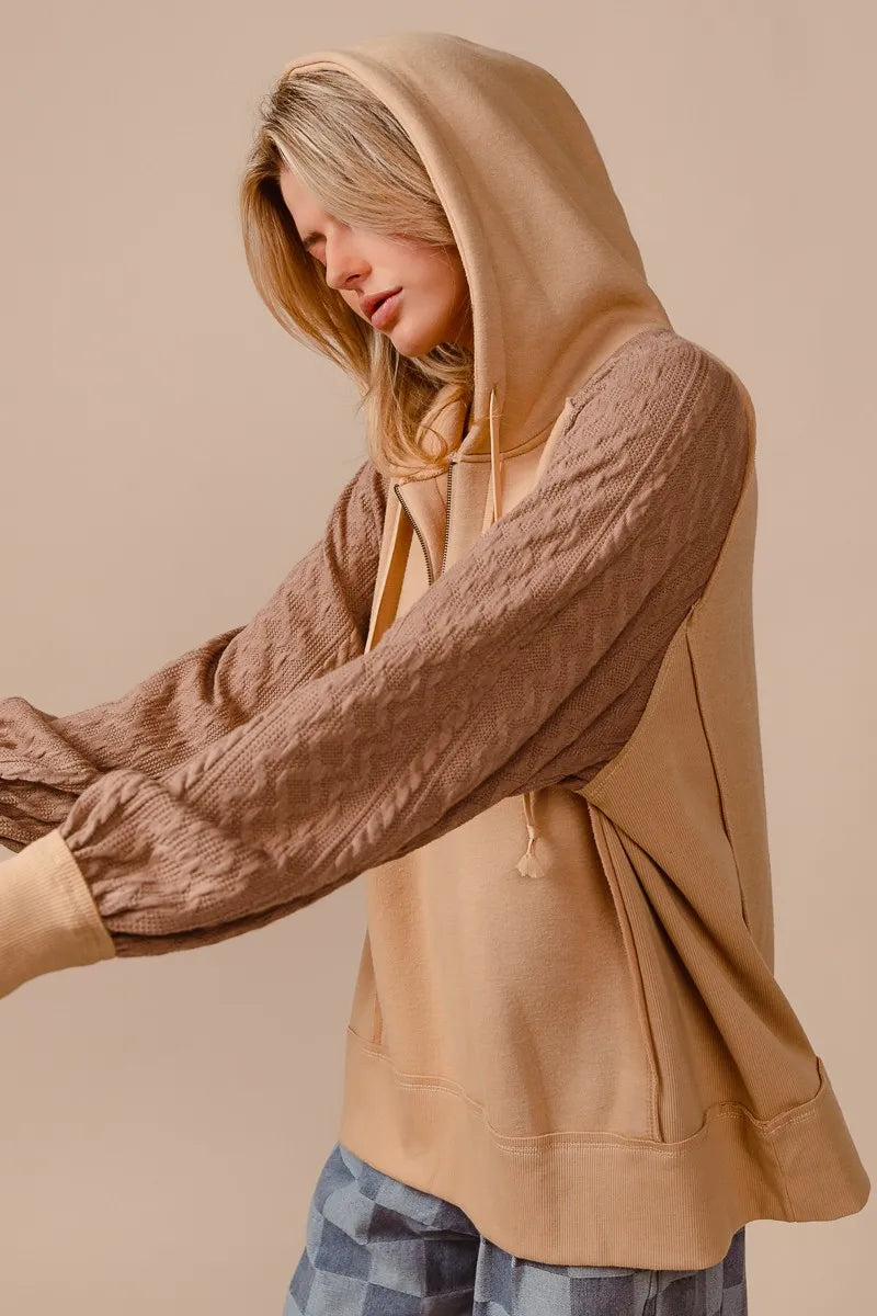 Woman wearing a beige French terry hoodie with knit sleeves and a half-zip front for a cozy, casual look.
