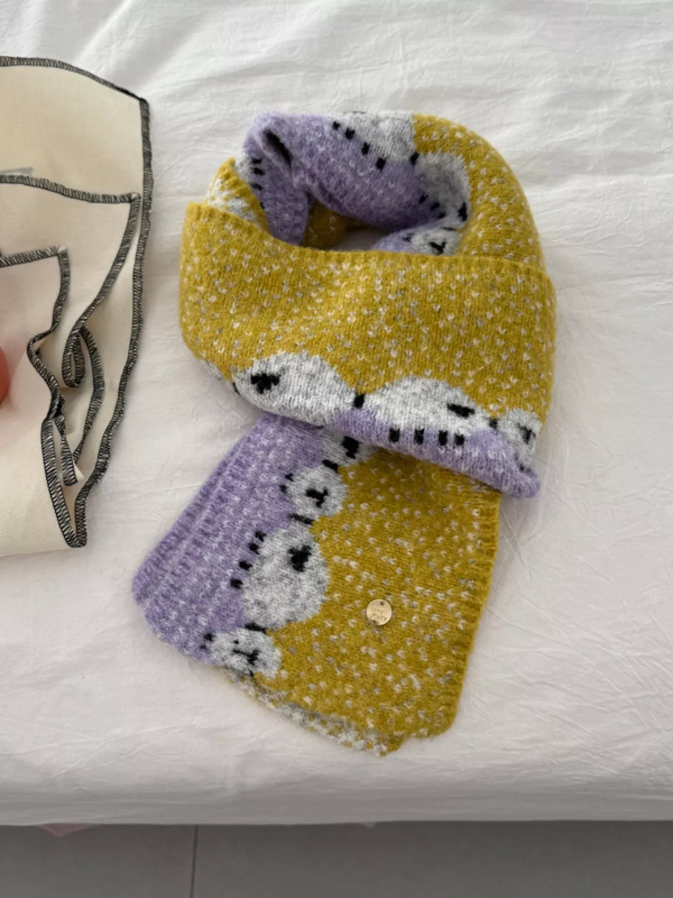 Soft knit scarf featuring a whimsical sheep pattern laid out on a neutral fabric background