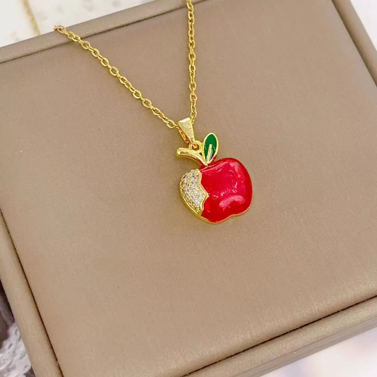Gold apple necklace with red enamel charm and crystal detail on chain