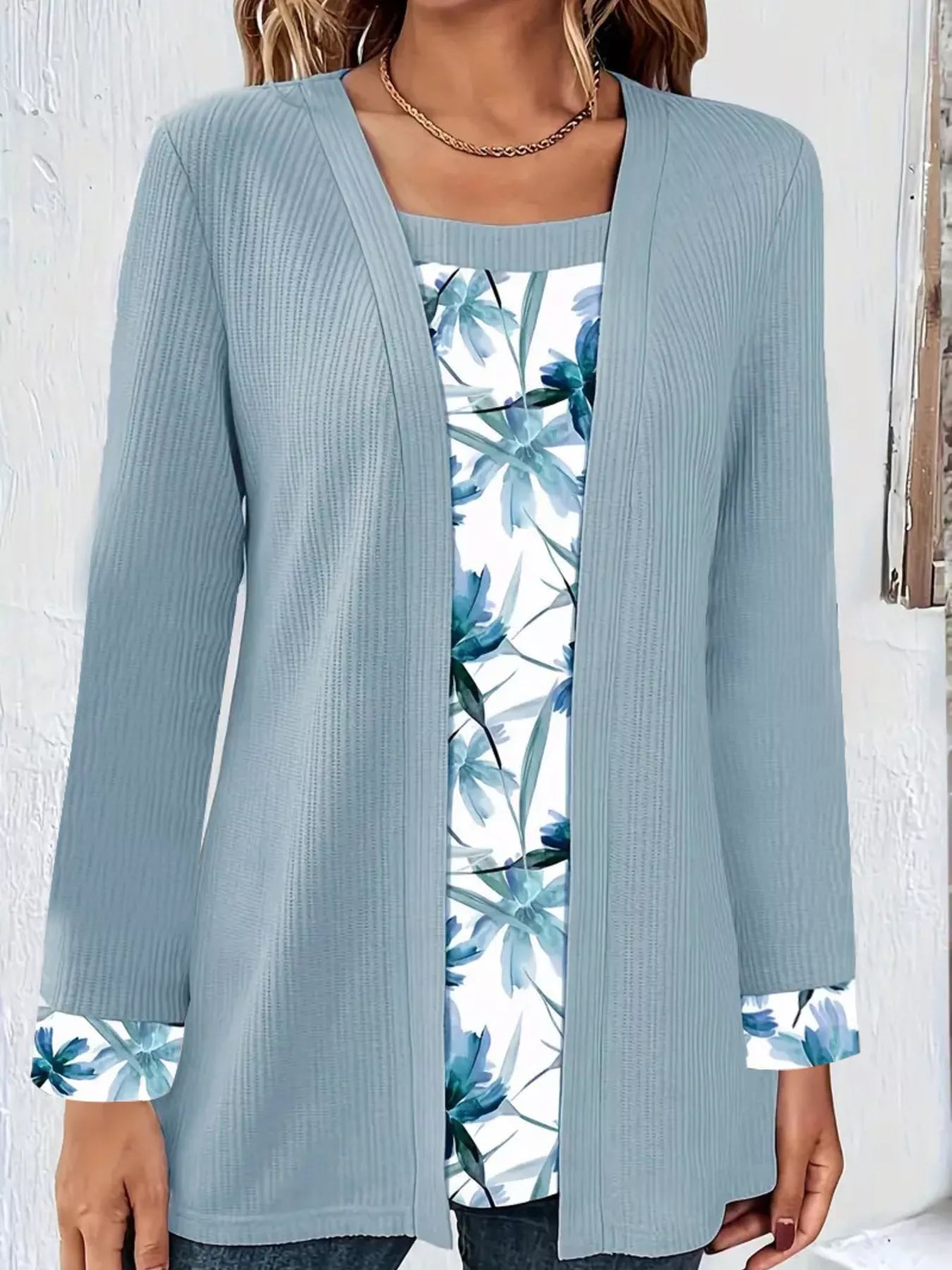 Woman wearing a faux two-piece top with a ribbed outer layer and floral underlayer at the neckline and sleeve cuffs.