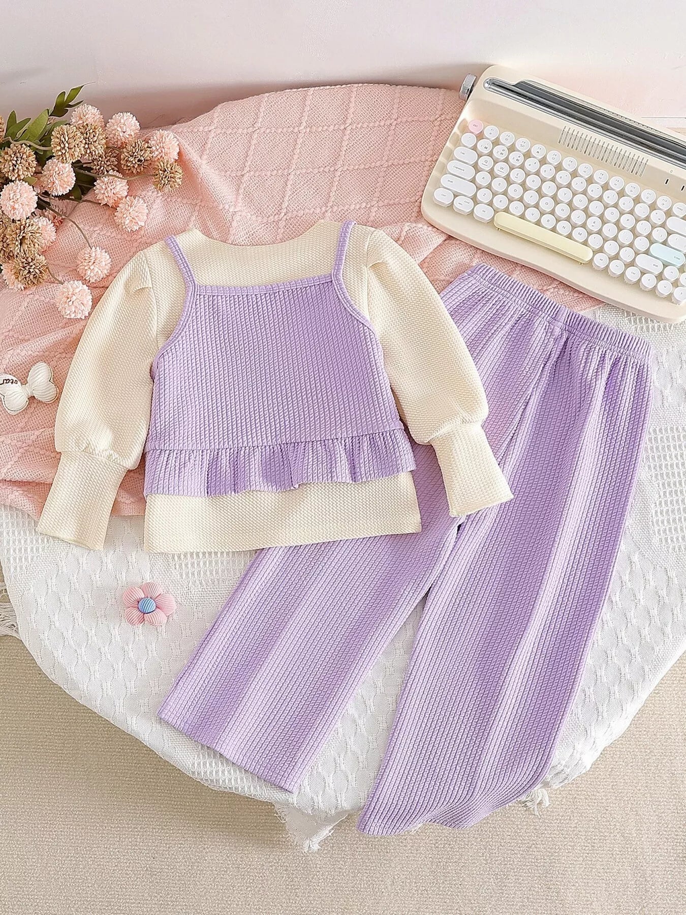 Children’s two-piece outfit with lavender ribbed pants, matching frill top, daisy appliqué details, and soft cotton-blend fabric.