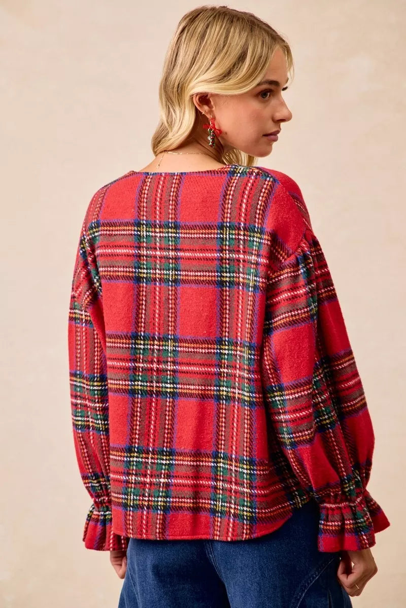 Woman wearing a festive red plaid button-front flounce-sleeve jacket with a v-neckline, styled for the holiday season.