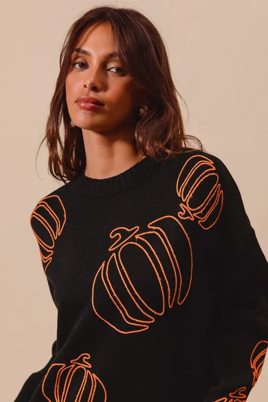 Woman wearing a black knit sweater with orange pumpkin outlines, styled with denim skirt — cozy Halloween pullover from A Whimsical Affair.
