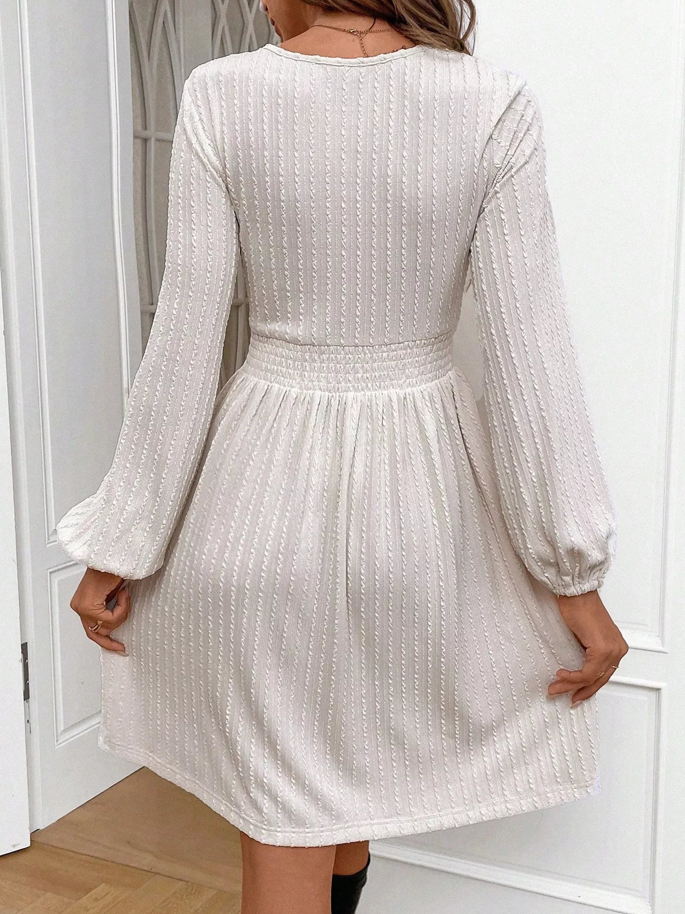 Cream long-sleeve textured mini dress with smocked waist worn indoors.