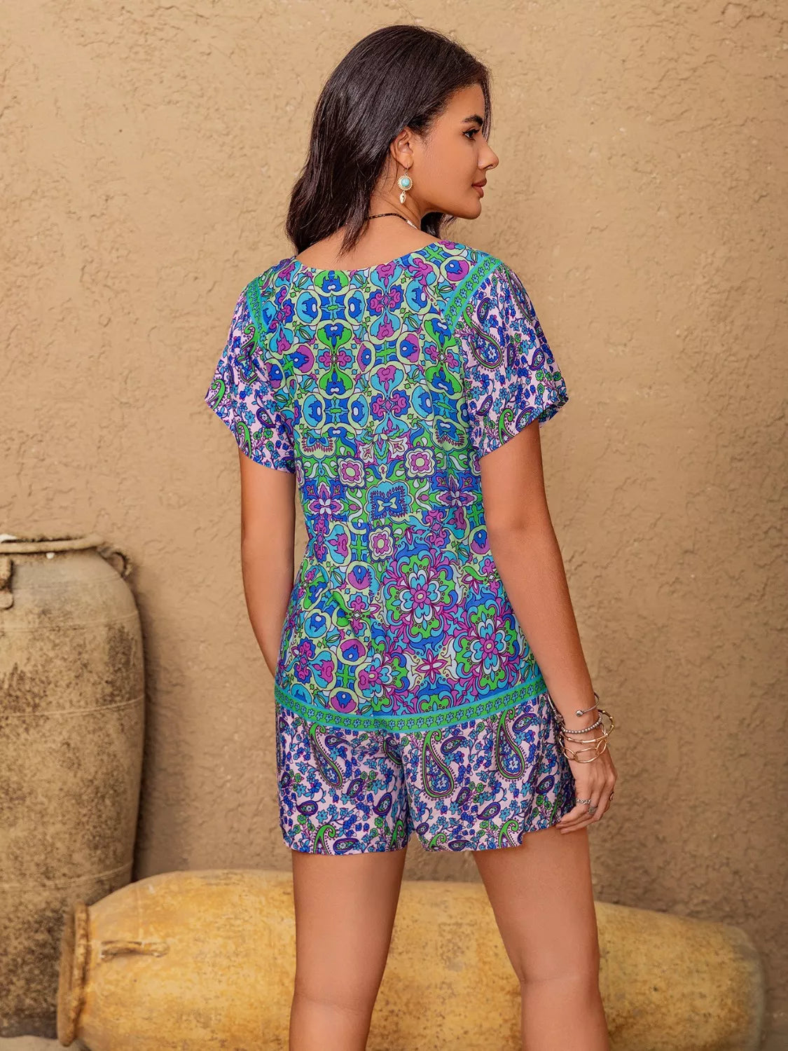 Woman wearing Mystic Meadow Romper with paisley and floral boho print in blue, purple, and green, tie-front detail, summer festival outfit.