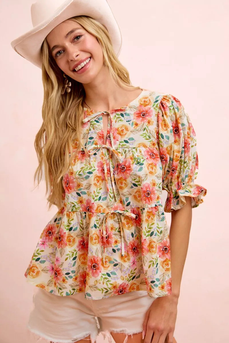 Floral cotton blouse with tie-front neckline, ruffled details, frill accents, puff sleeves, and soft romantic cottage style.