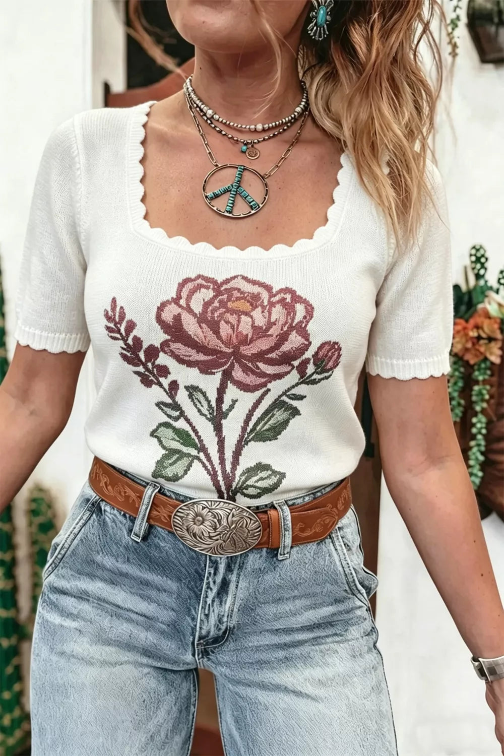 White short sleeve knit top with a large rose design, scalloped neckline, seam detail, and slightly stretchy fit styled with denim jeans.