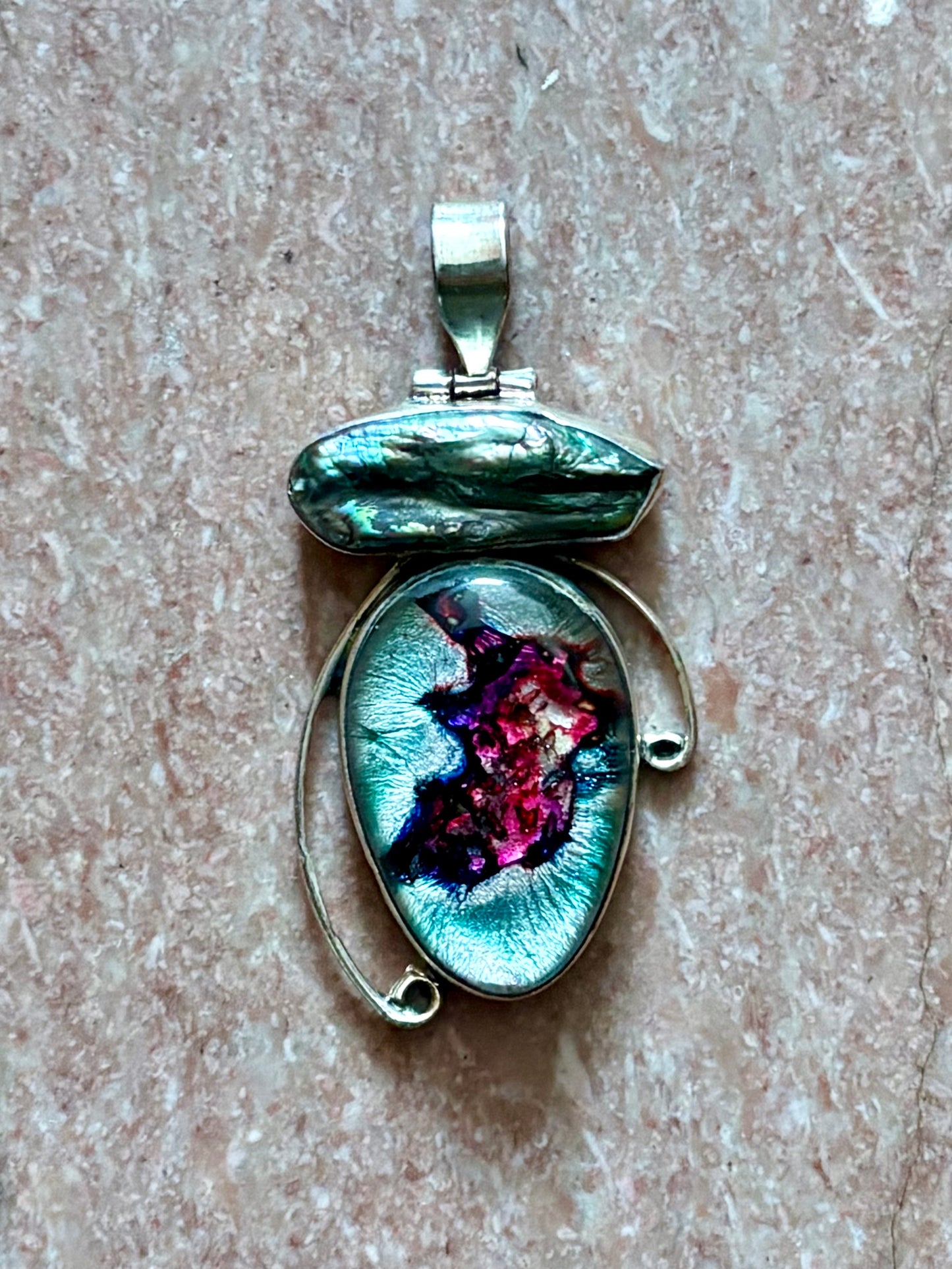 Dichroic glass and pearl pendant with silver-toned setting and shifting magenta and teal tones on a blue background