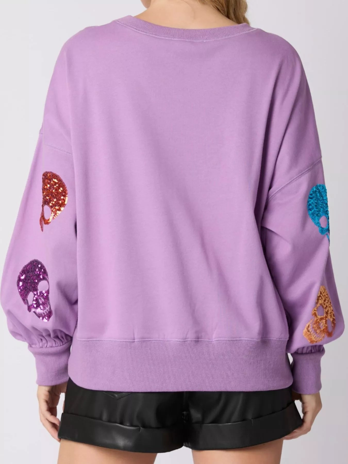 Woman wearing a lavender sweatshirt with colorful sequin skulls — statement Halloween top with a glam twist from A Whimsical Affair.