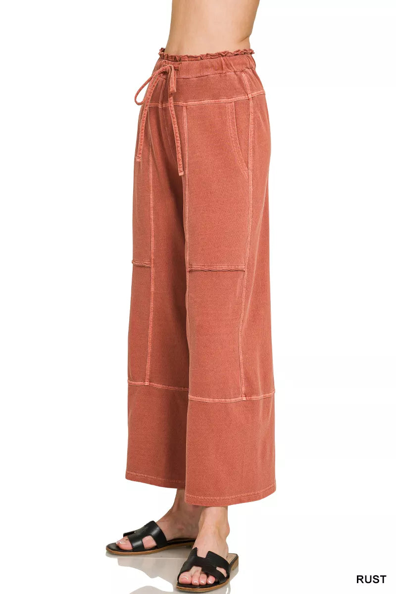 Rust wide-leg French terry pants with drawstring waist, exposed seam details, pockets, and relaxed casual fit.