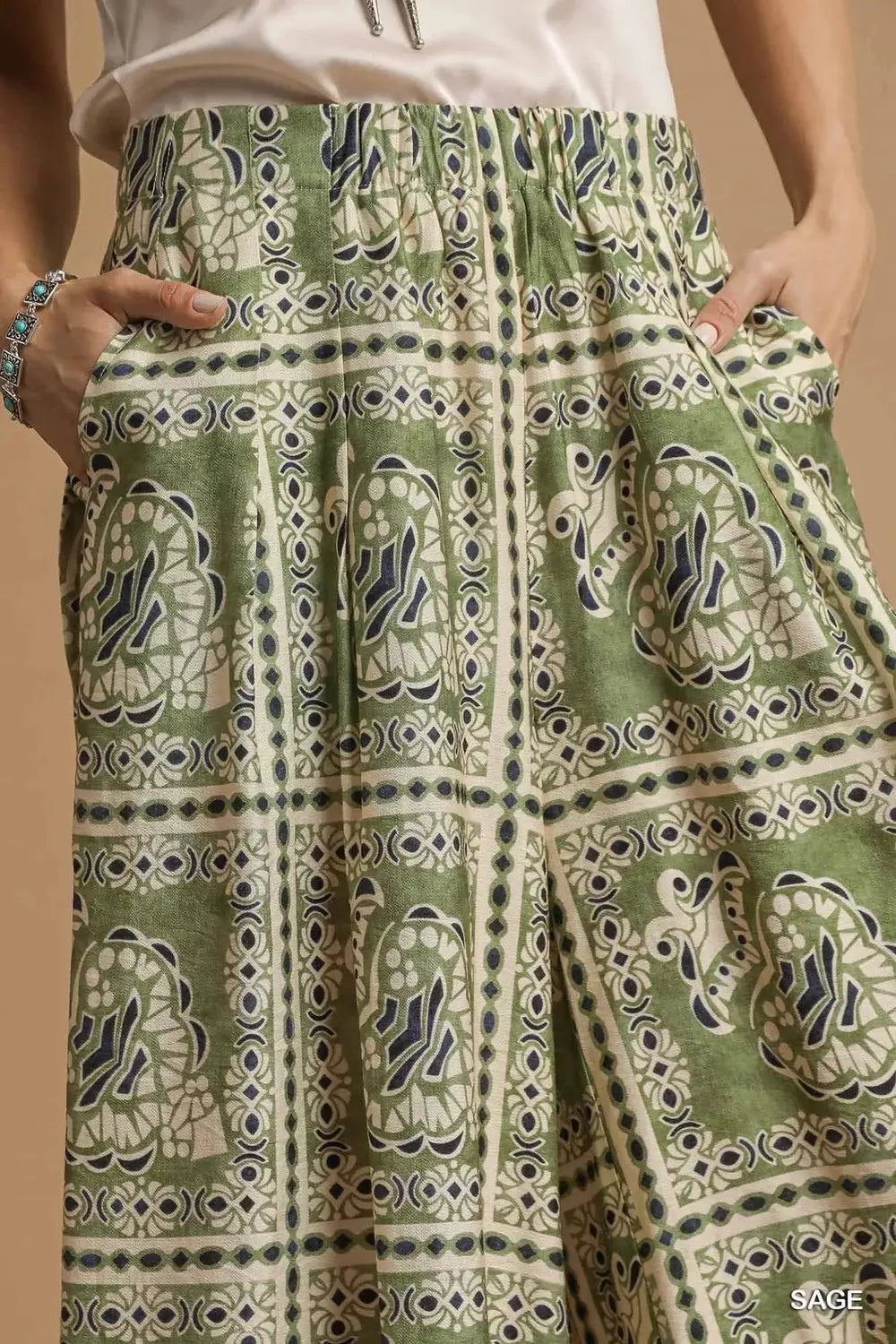 Model wearing Sage Mosaic Boho Pants with sage-toned bohemian print, wide-leg silhouette, and functional side pockets styled with boots.