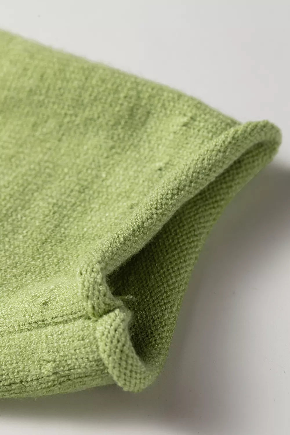 Green knit sweater with a blue fish graphic, ribbed detail, long sleeves, and relaxed slightly stretchy fit styled with white pants.