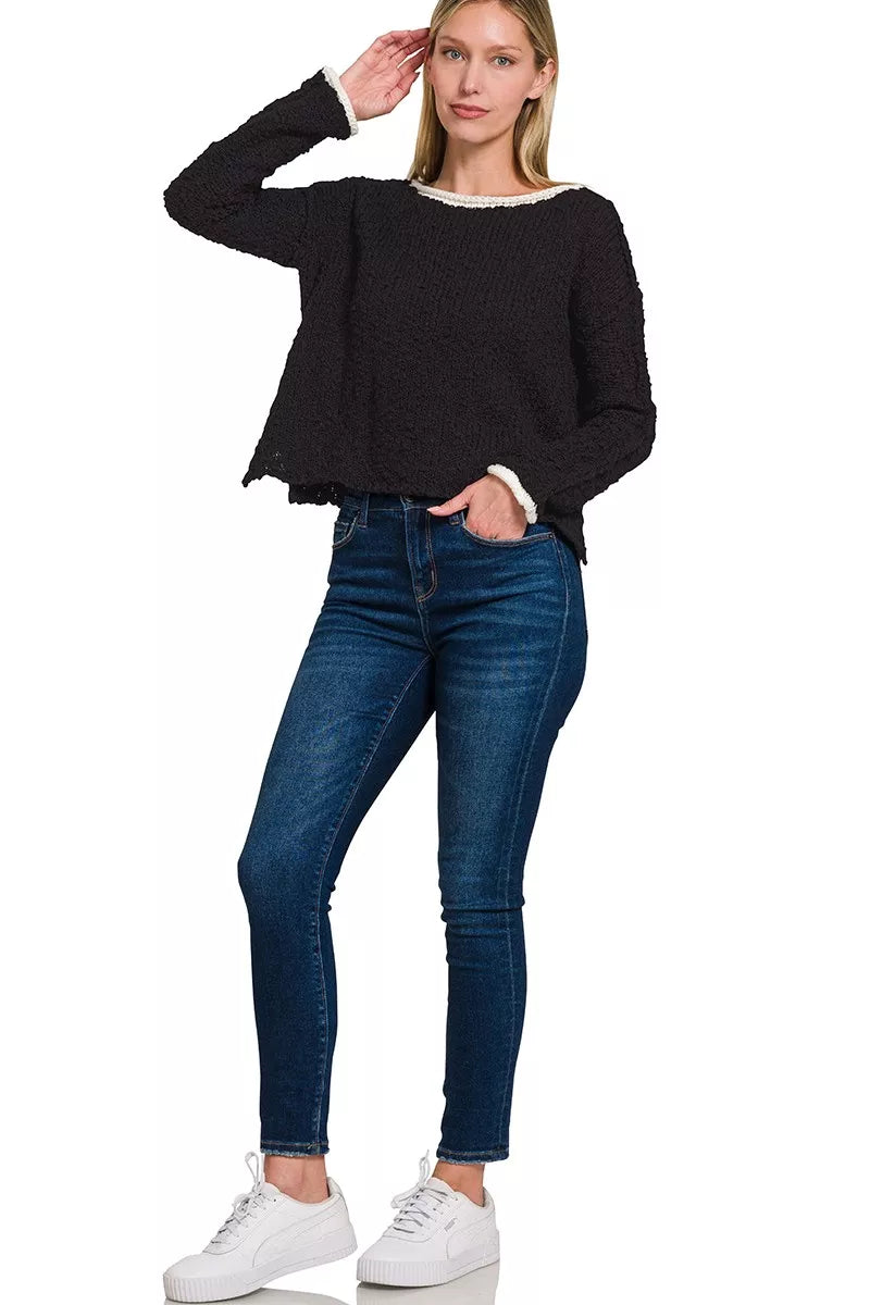 Model wearing the Solar Eclipse Contrast Sweater — a black textured cropped knit with ivory trim on the neckline and cuffs, styled with denim jeans.