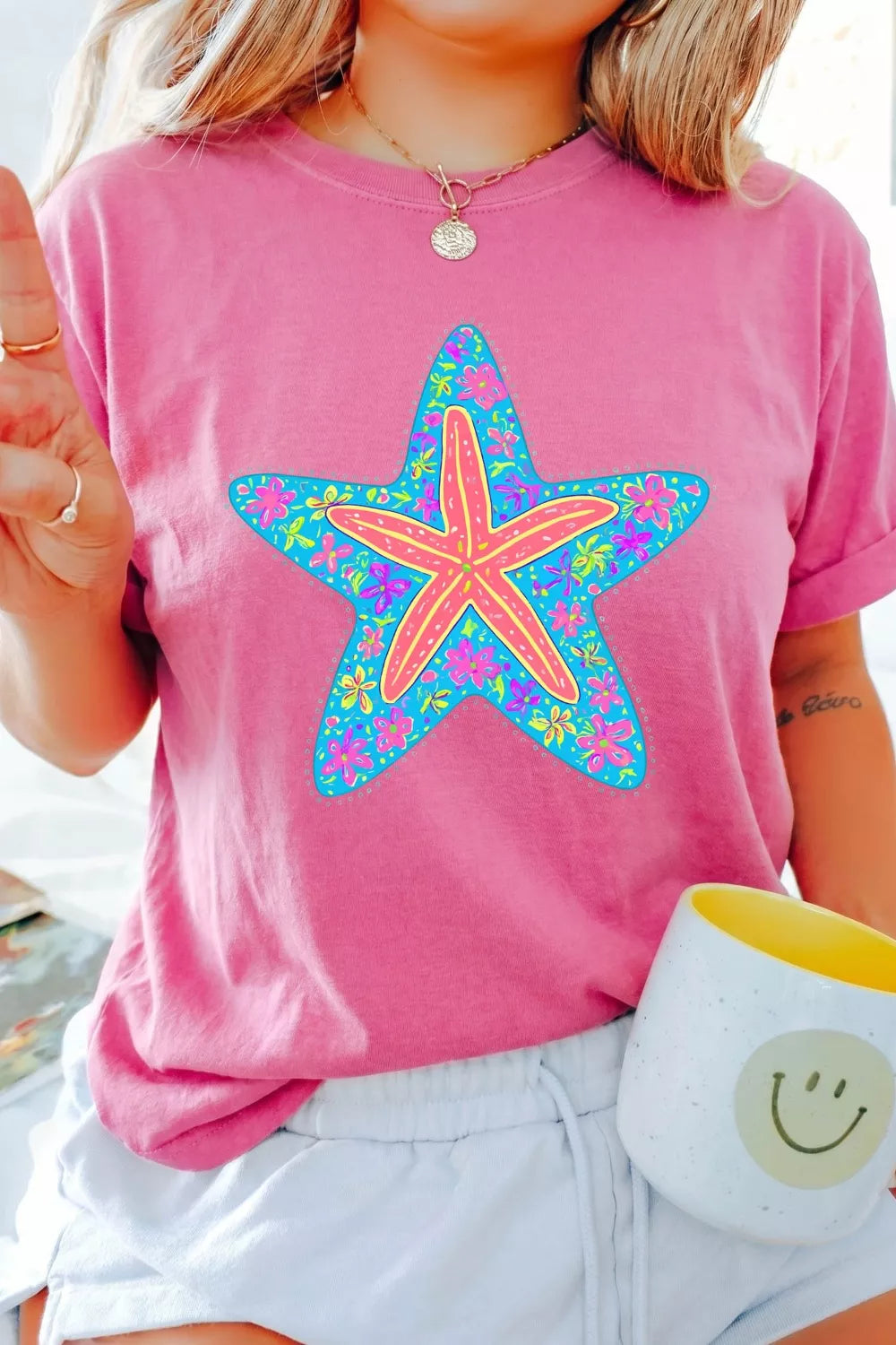 Bright pink short sleeve graphic tee with a colorful floral starfish design on the front, styled with light wash denim jeans.