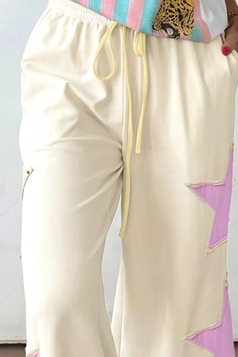 Cream wide leg pants with pastel star patch details, drawstring waist, pockets, and soft cotton-blend fabric styled with sneakers.