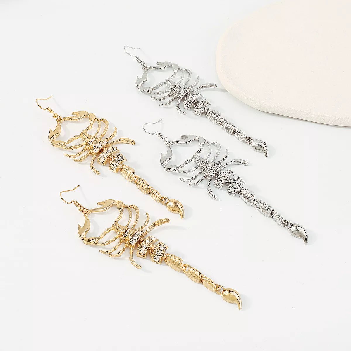 Gold and silver scorpion-shaped rhinestone statement earrings with ribbed detailing displayed on a white surface.