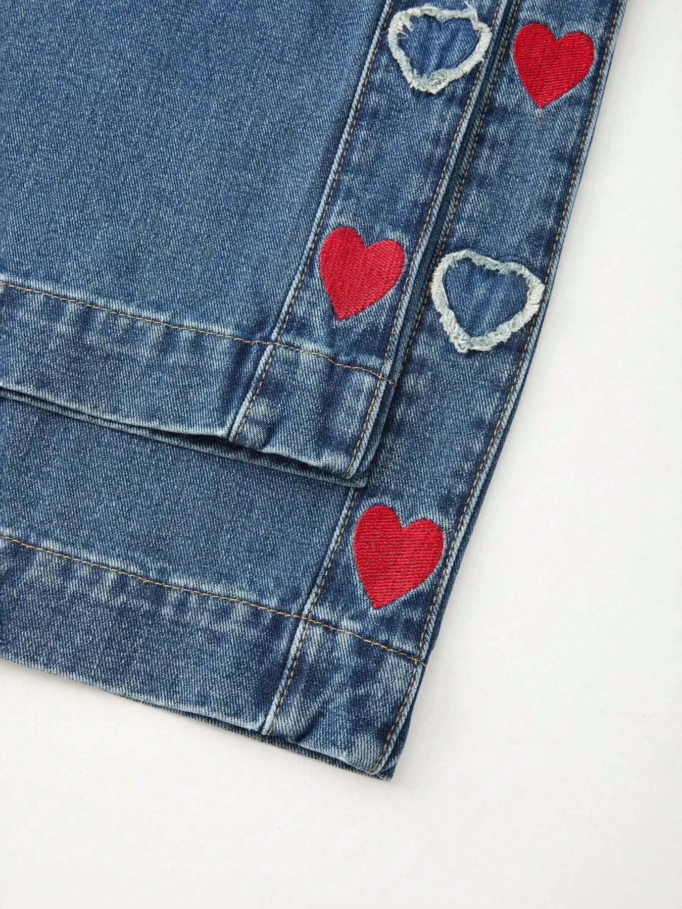 Relaxed denim pants with embroidered red and white heart details along the side panels, elastic waistband, and cuffed hems.