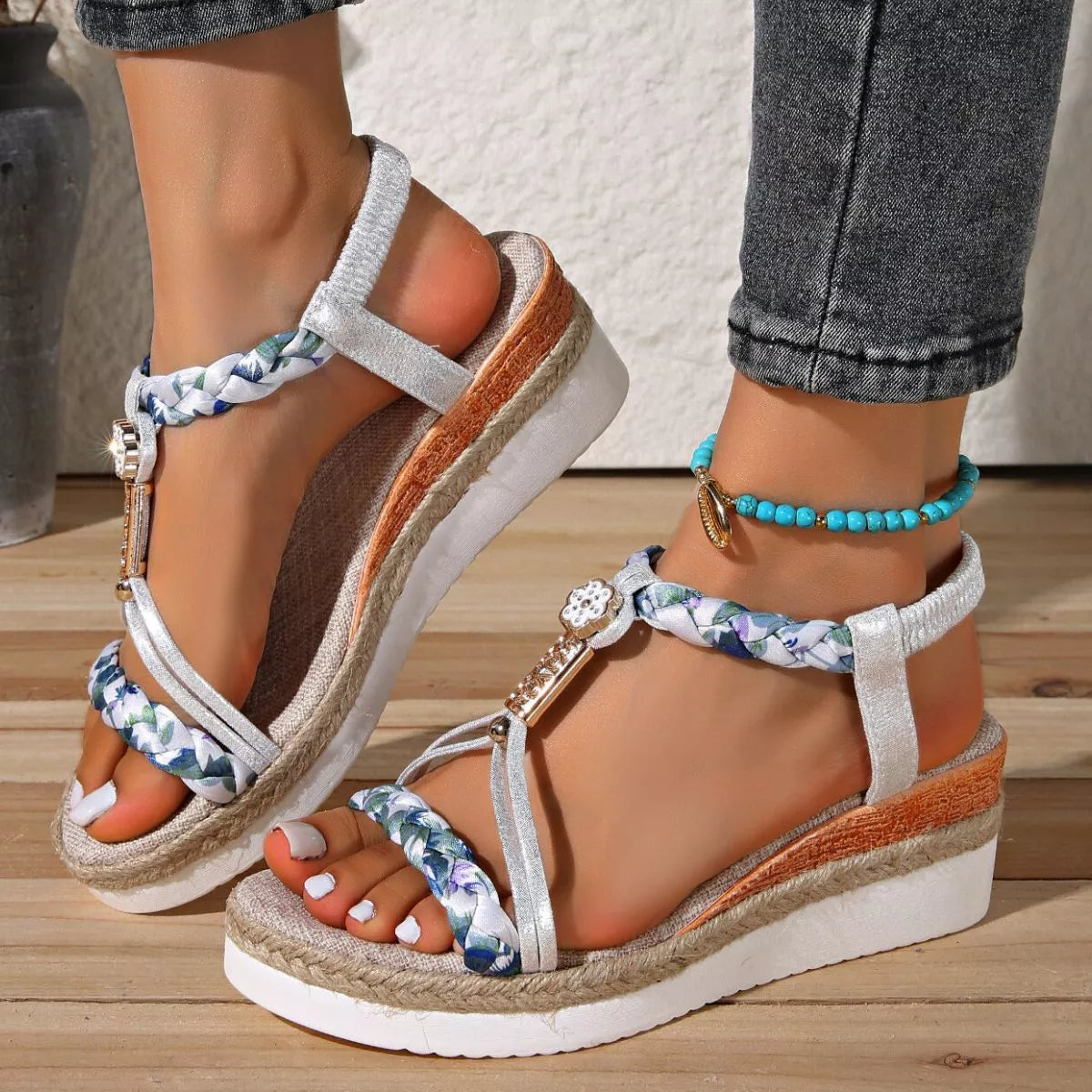 Boho open-toe wedge sandals with colorful braided straps, decorative charm details, low heel, and rubber sole styled with white pedicure.