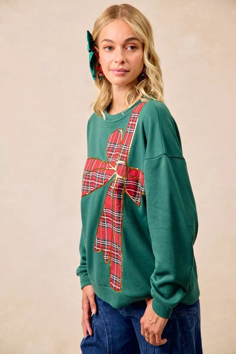 Woman wearing a green fleece pullover with a large red plaid bow design — festive holiday top from A Whimsical Affair.