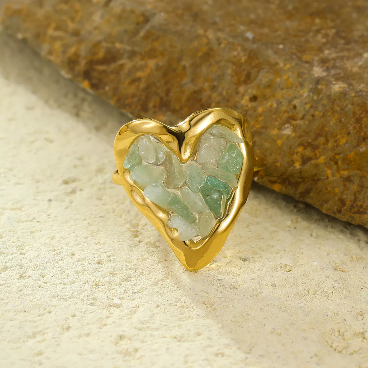 Gold heart ring with gum leaf green fluorite stones, displayed near a textured rock.