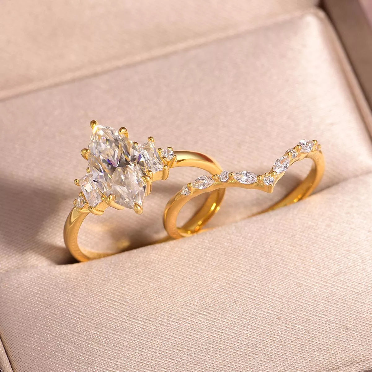 Close-up of a gold-plated two-piece moissanite ring set featuring a marquise-cut center stone with baguette accents and a curved zircon band.