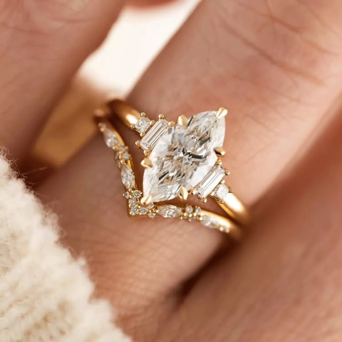 Close-up of a gold-plated two-piece moissanite ring set featuring a marquise-cut center stone with baguette accents and a curved zircon band.