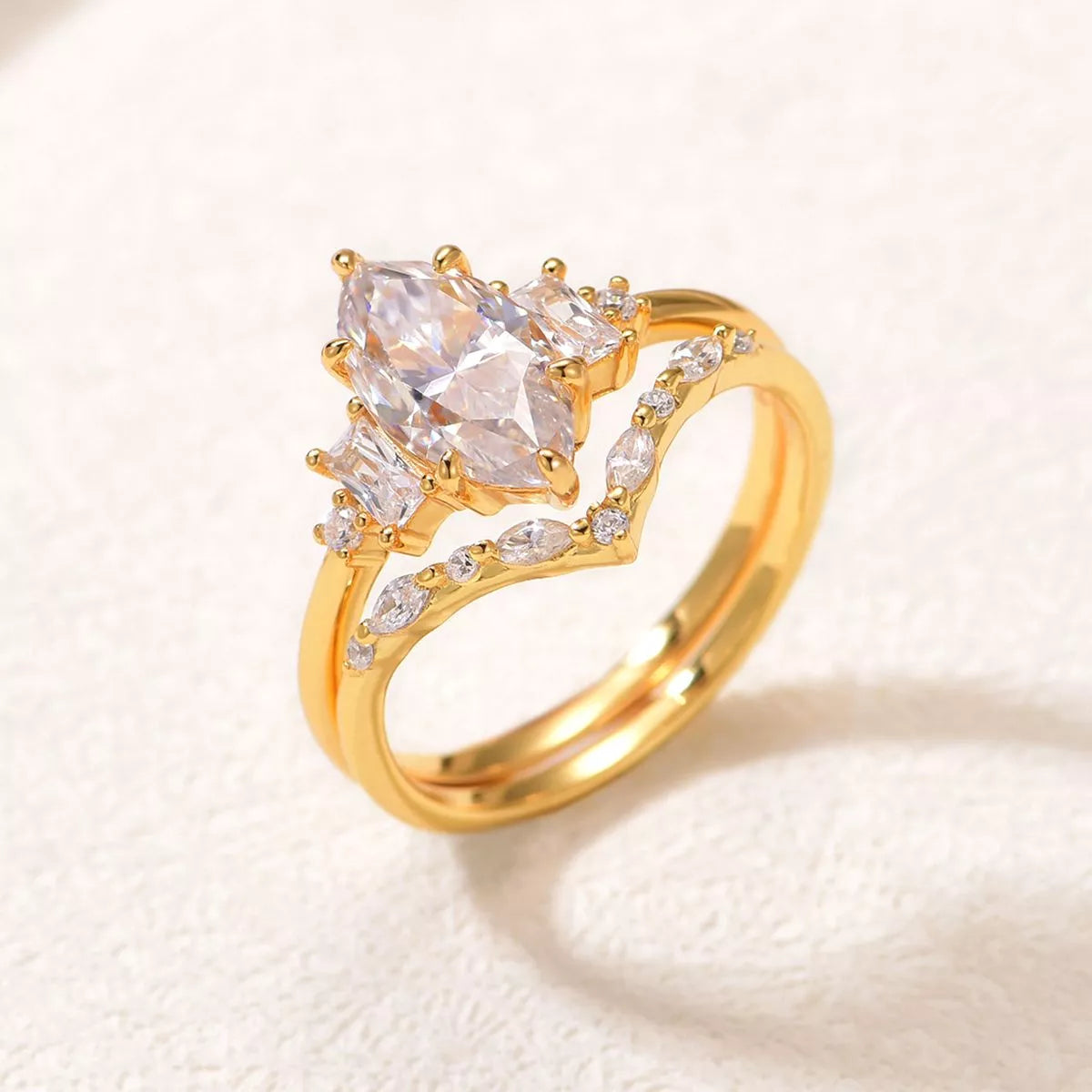 Close-up of a gold-plated two-piece moissanite ring set featuring a marquise-cut center stone with baguette accents and a curved zircon band.