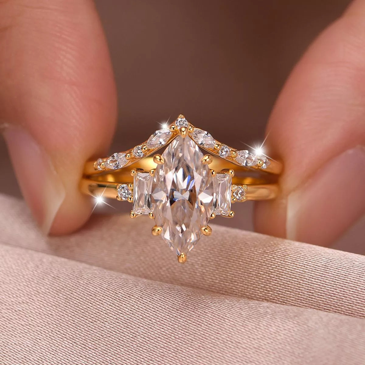 Close-up of a gold-plated two-piece moissanite ring set featuring a marquise-cut center stone with baguette accents and a curved zircon band.