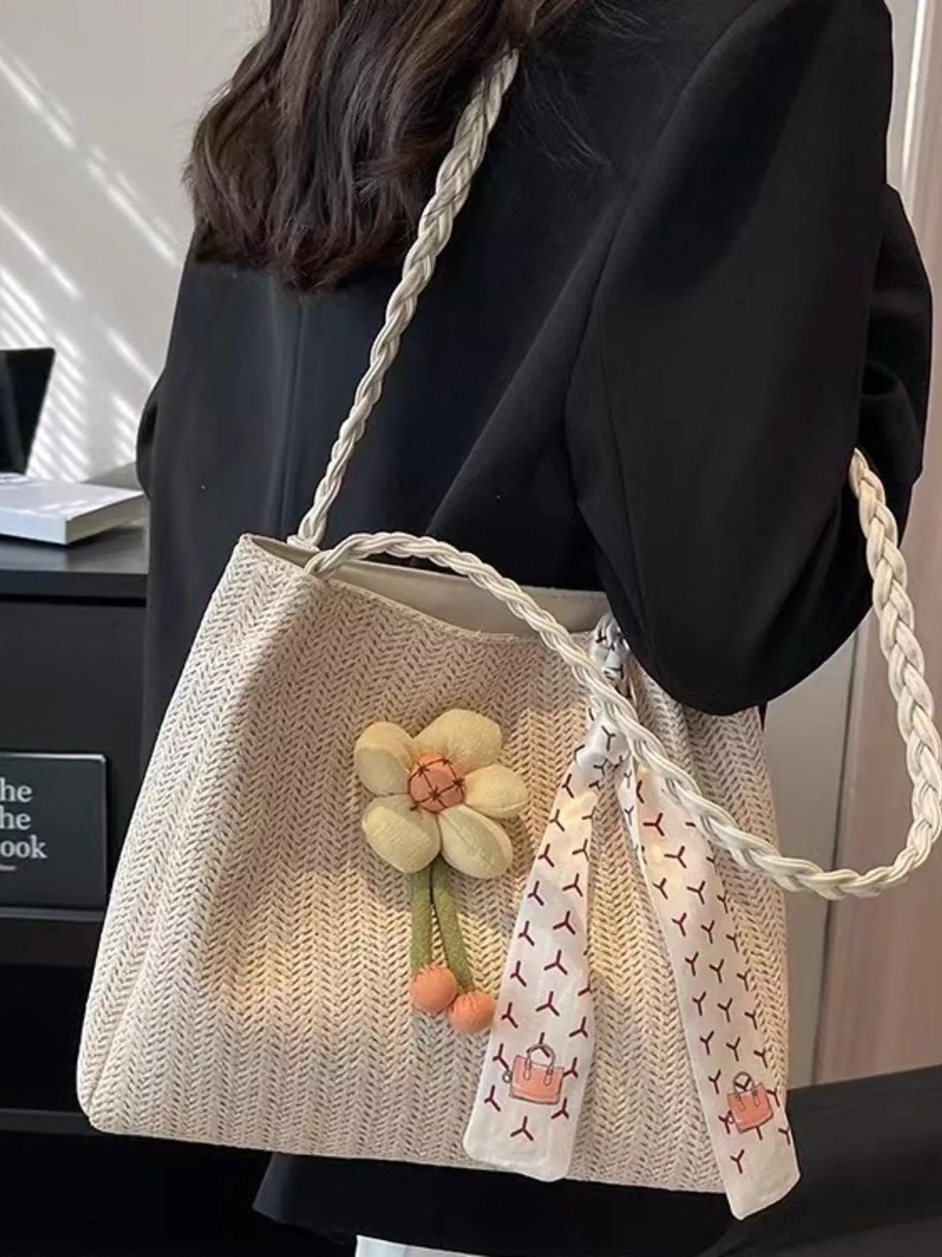 Beige woven straw tote bag with braided handles, a plush decorative flower, and a printed scarf detail