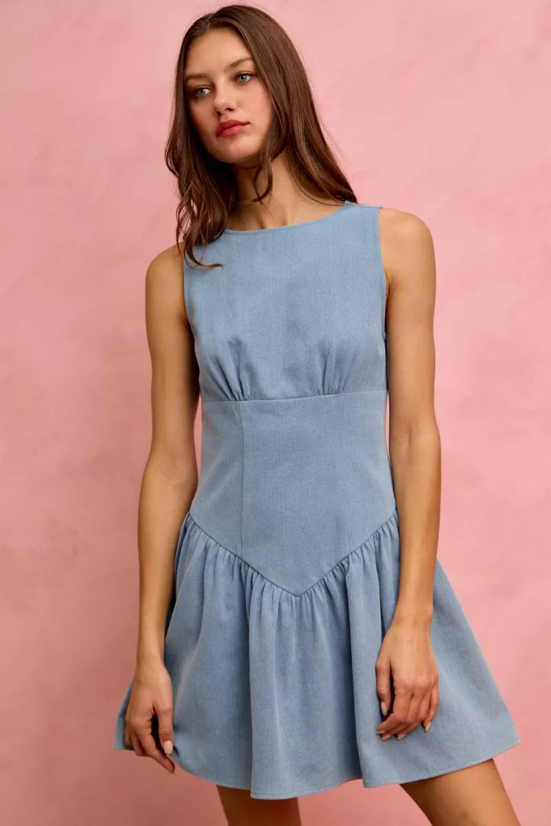 Model wearing a sleeveless fit and flare denim mini dress with structured bodice and flared skirt against a pink backdrop.