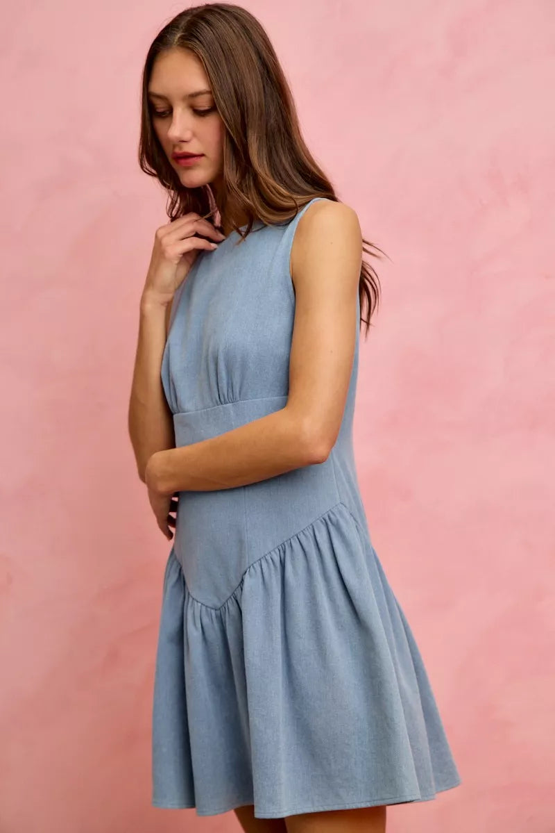 Model wearing a sleeveless fit and flare denim mini dress with structured bodice and flared skirt against a pink backdrop.