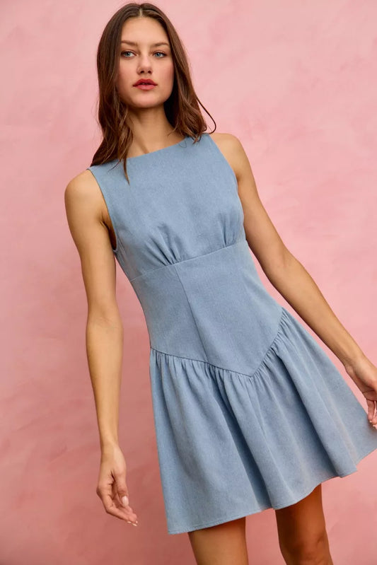 Model wearing a sleeveless fit and flare denim mini dress with structured bodice and flared skirt against a pink backdrop.