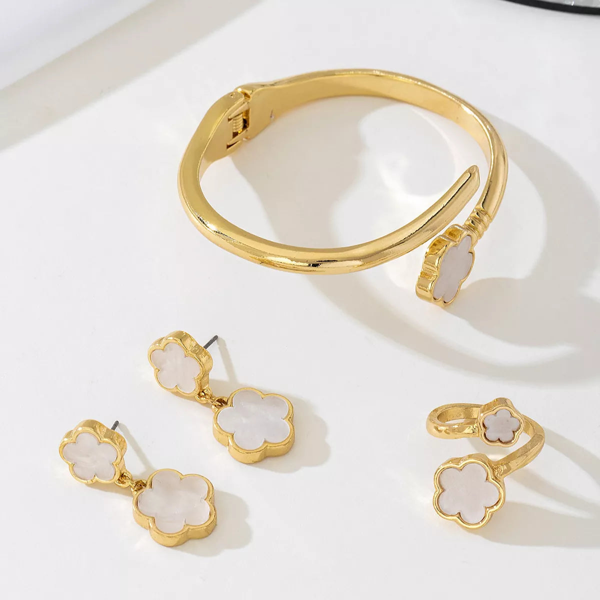 Matching gold-plated white clover jewelry set including earrings, bracelet, and ring — elegant minimalist design.
