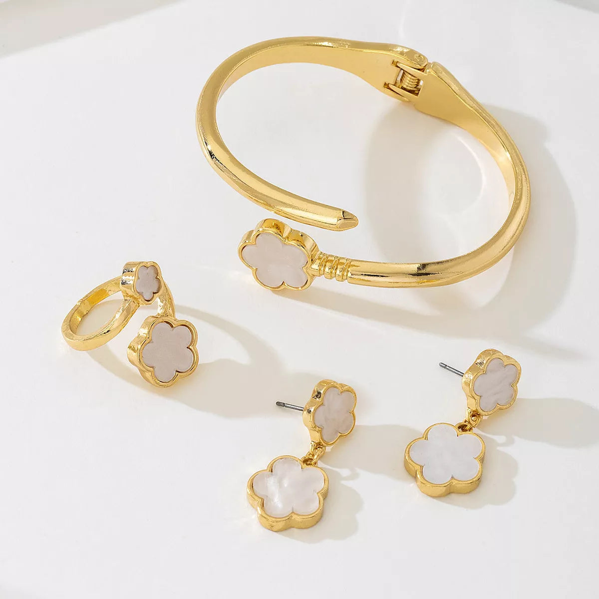Matching gold-plated white clover jewelry set including earrings, bracelet, and ring — elegant minimalist design.