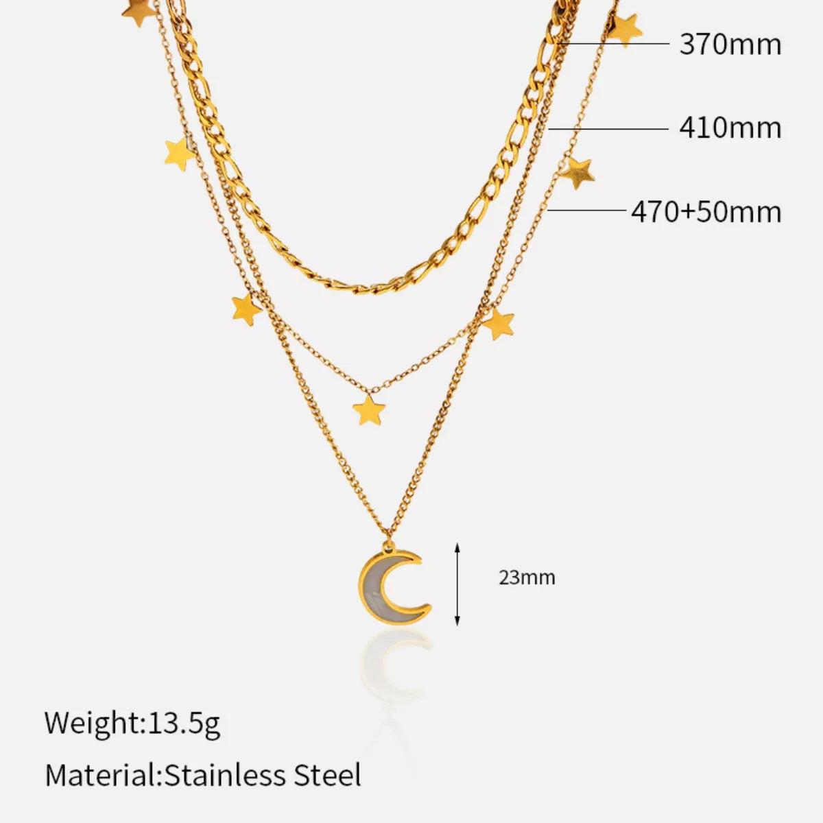 Gold layered necklace with three chains featuring small star charms and a crescent moon pendant displayed on a textured beige background.