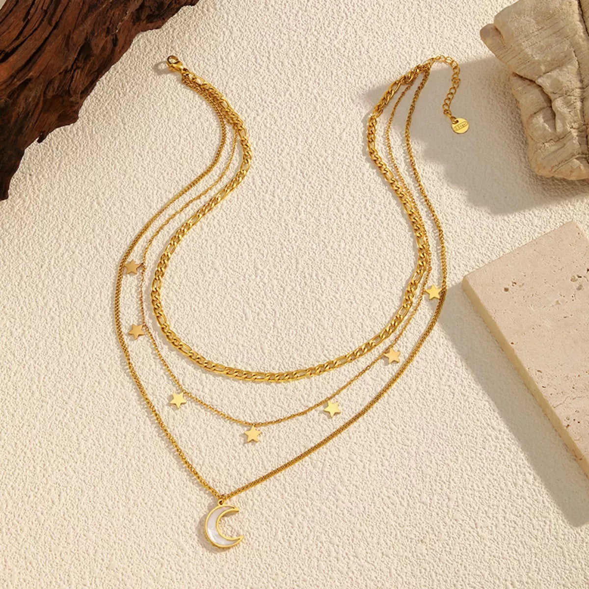 Gold layered necklace with three chains featuring small star charms and a crescent moon pendant displayed on a textured beige background.