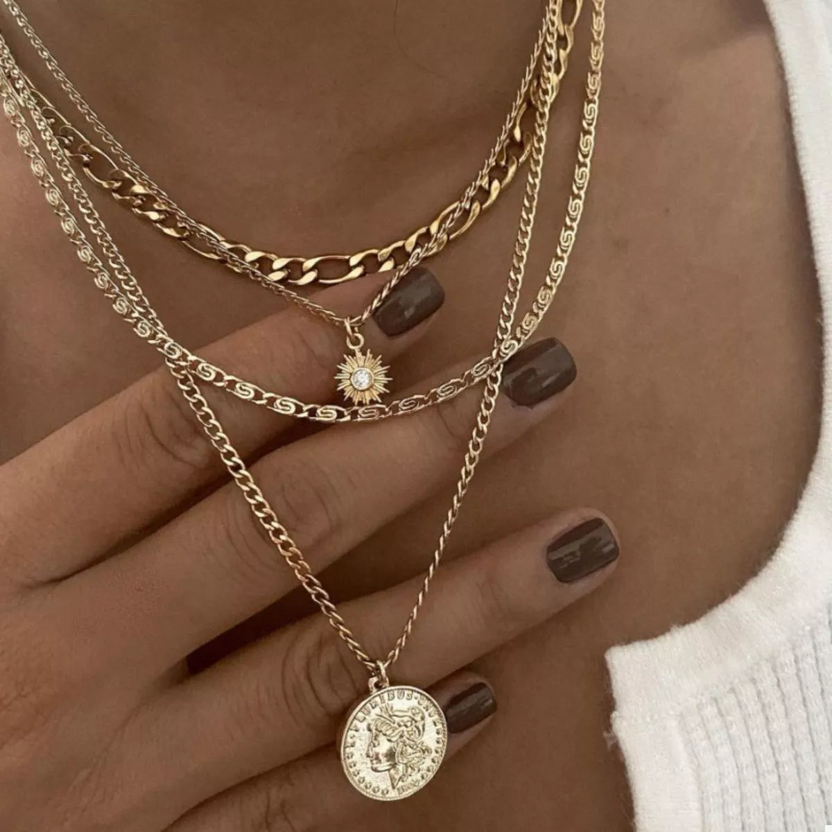 Celestial layered necklace stack with vintage coin charm and radiant sun pendant
