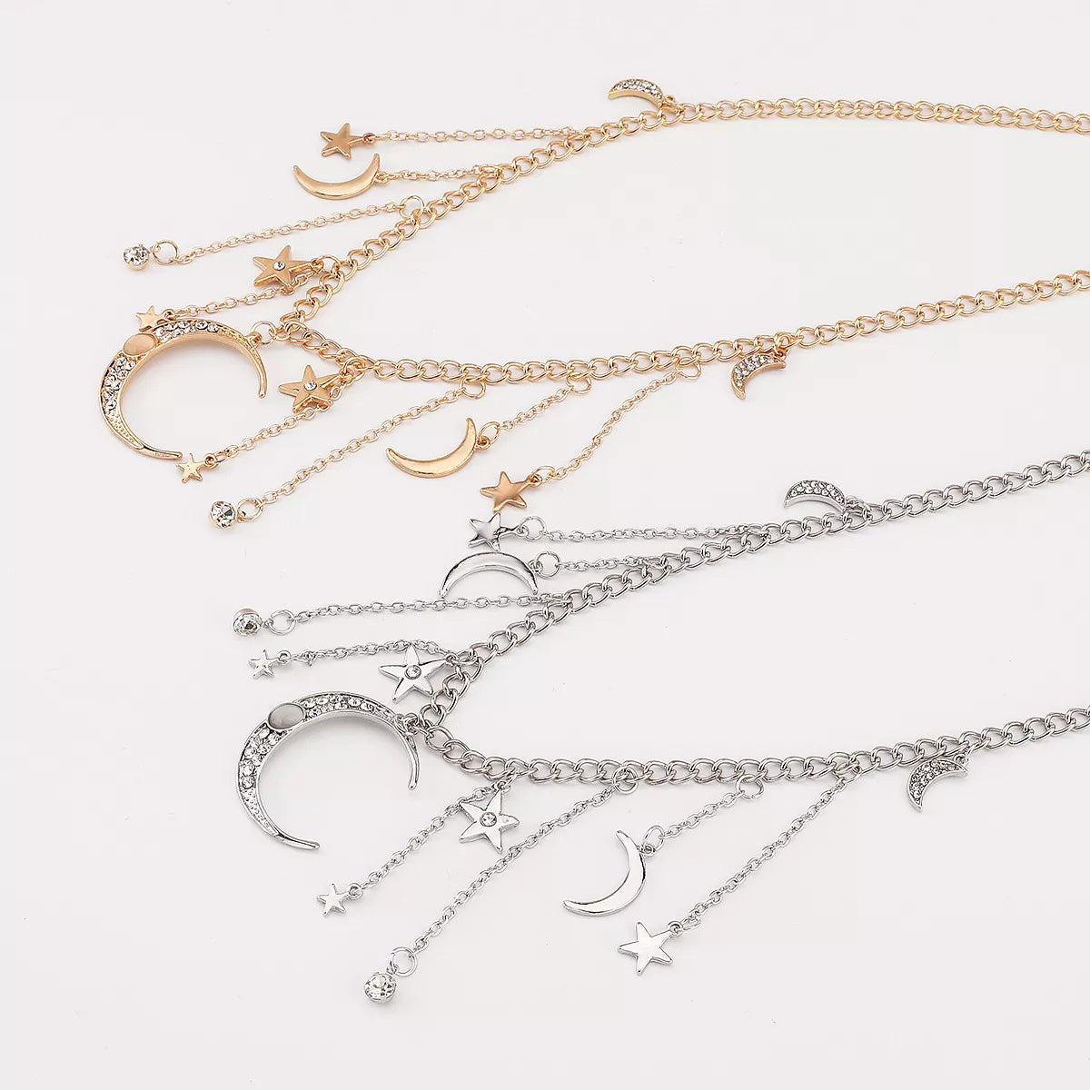 Gold and silver celestial necklaces featuring dangling moon, star, and rhinestone charms arranged on chain links.