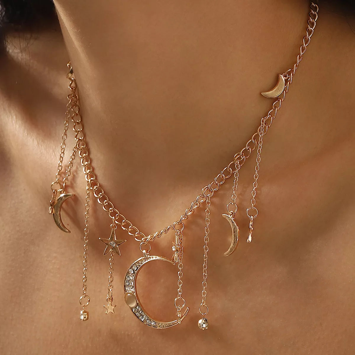 Gold and silver celestial necklaces featuring dangling moon, star, and rhinestone charms arranged on chain links.
