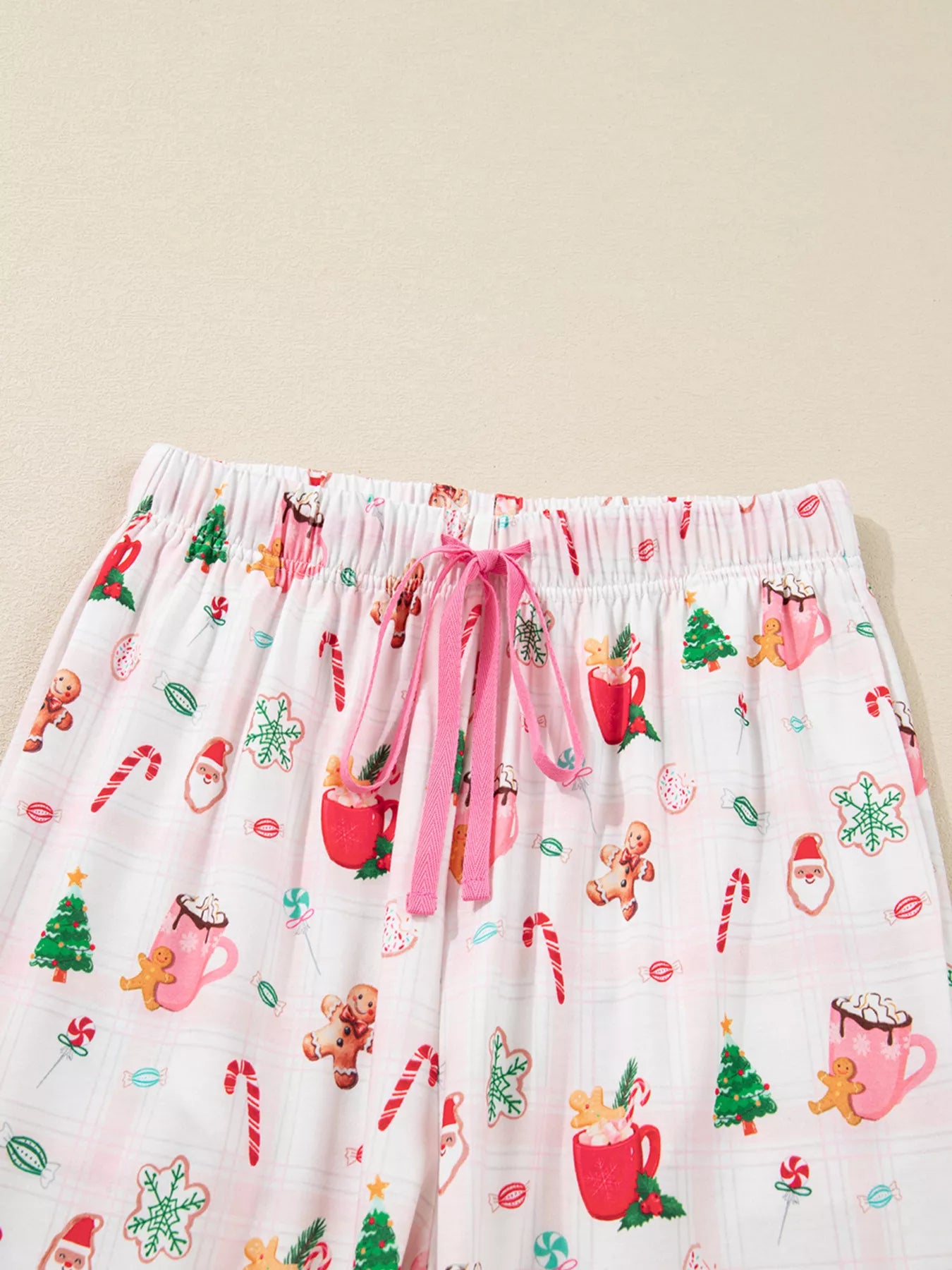 Close-up of holiday printed pajama pants featuring candy canes, cocoa mugs, gingerbread cookies, and Santa motifs.