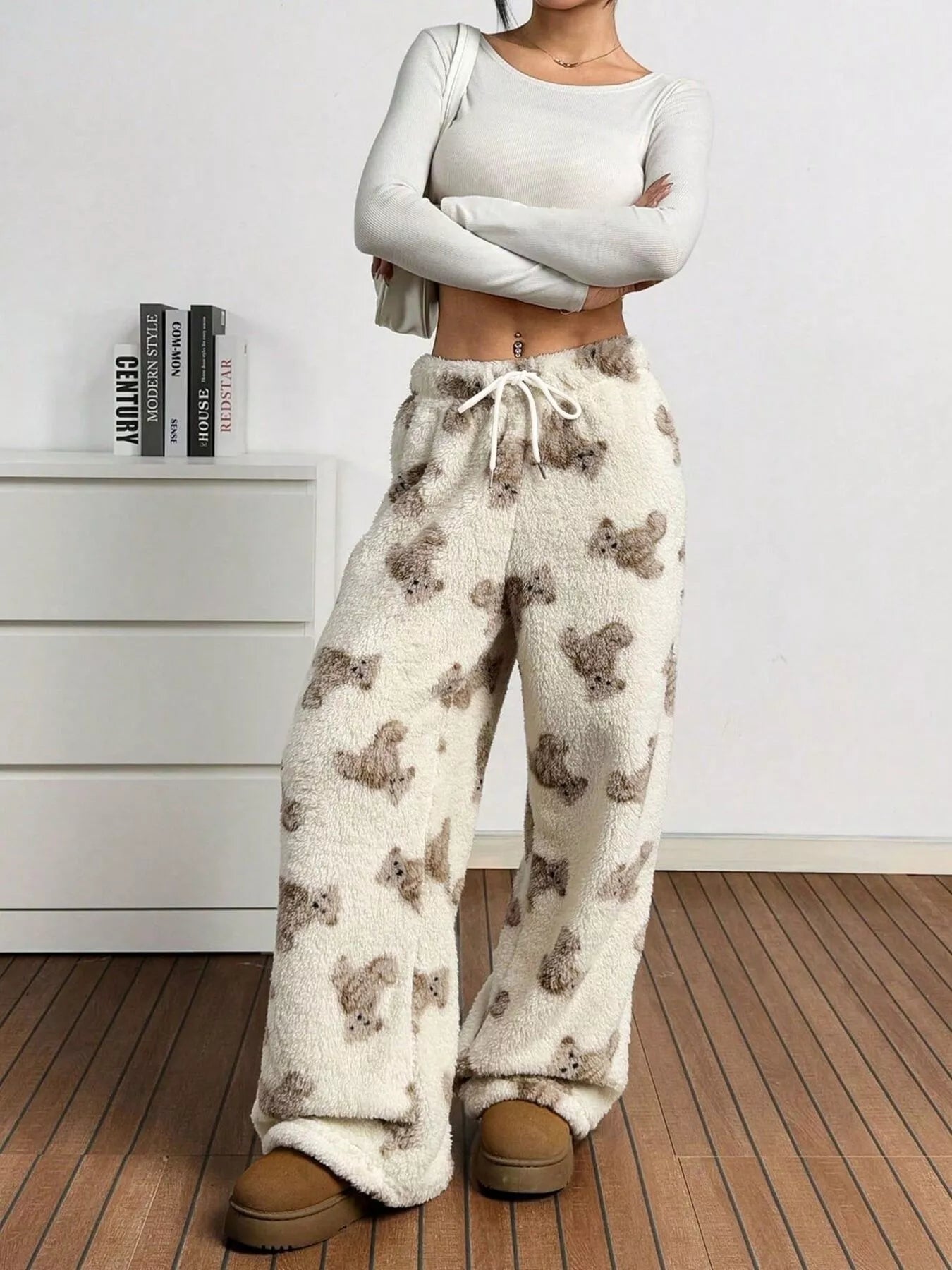 Cream fuzzy teddy bear print lounge pants with drawstring waist, styled with cozy slippers in a modern indoor setting.